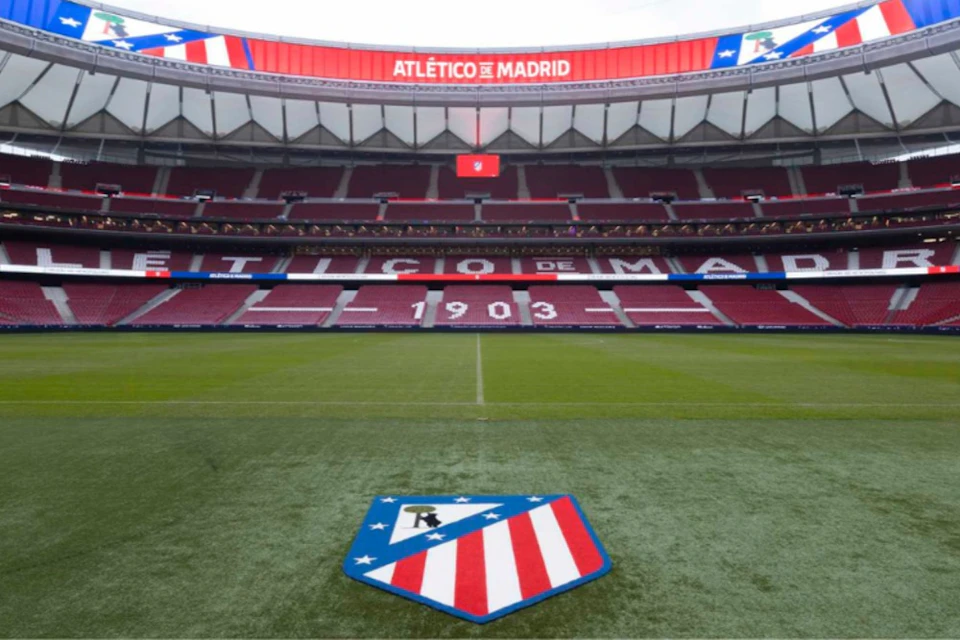 View of a football stadium with red seats, a large logo on the field, and a screen displaying "Atlético de Madrid."