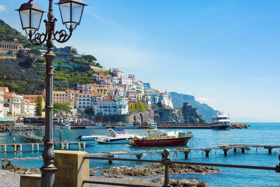 港口场景，船只在水中，山坡上有五颜六色的建筑，晴朗的蓝天。 前景中的灯柱。