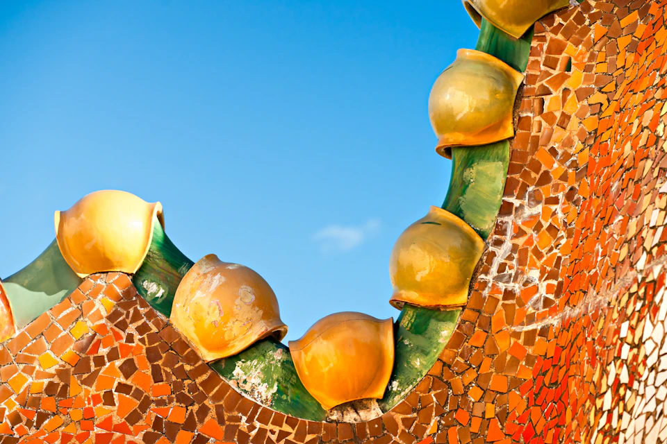 Close-up of a building's curved roof adorned with mosaic tiles and yellow ceramic elements against a clear blue sky.