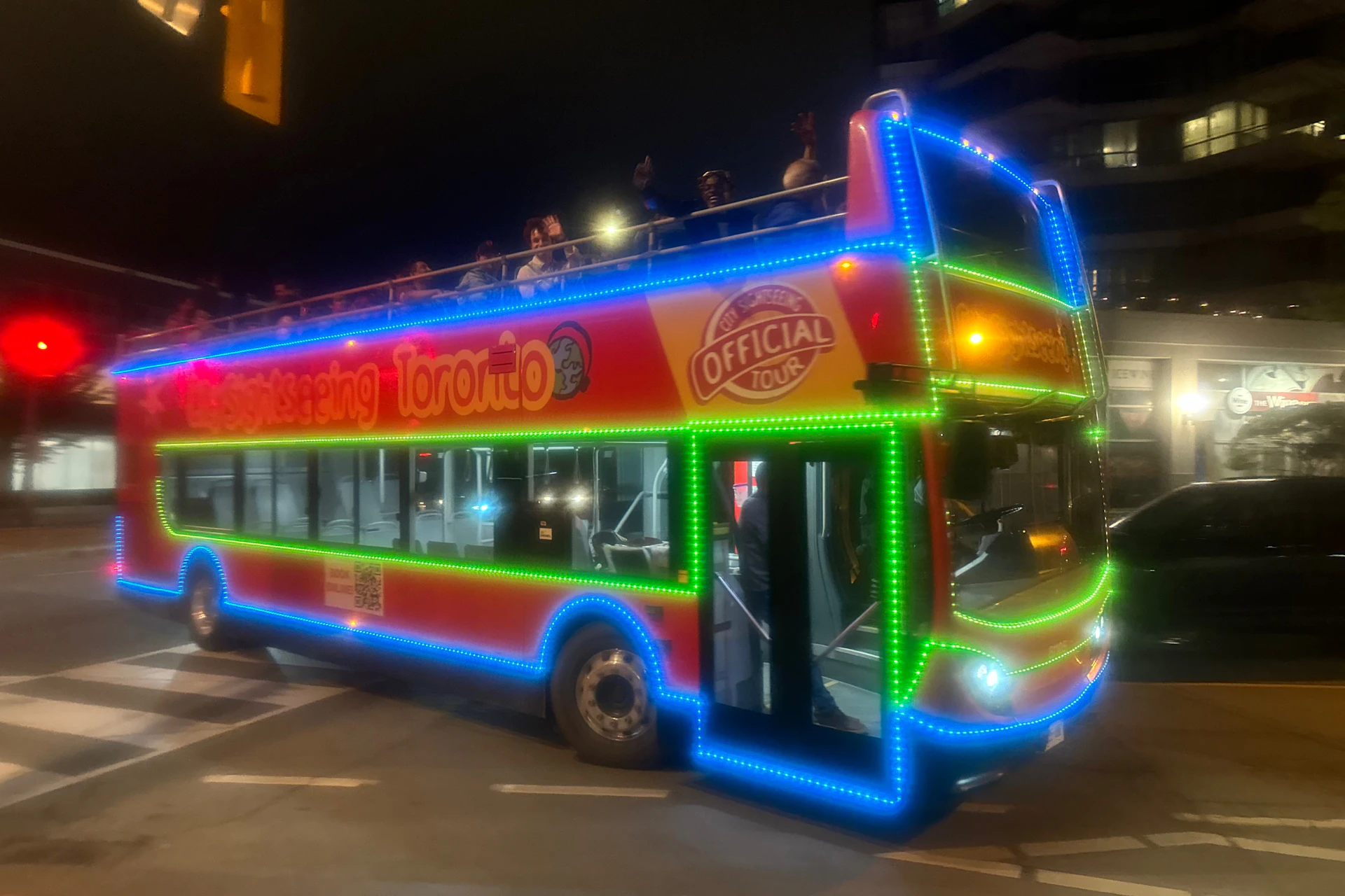 Open top double decker bus turning a corner at night time. Bus is covered with LED lights