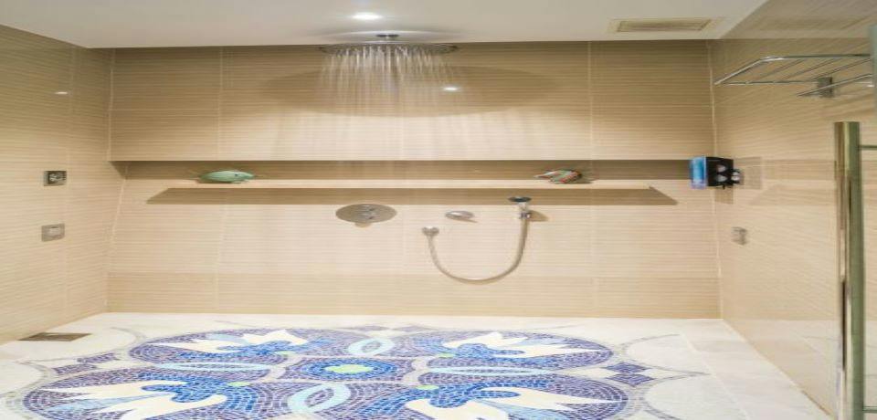 A modern shower with beige tiled walls, a rain showerhead, a handheld shower, and a mosaic tiled floor.