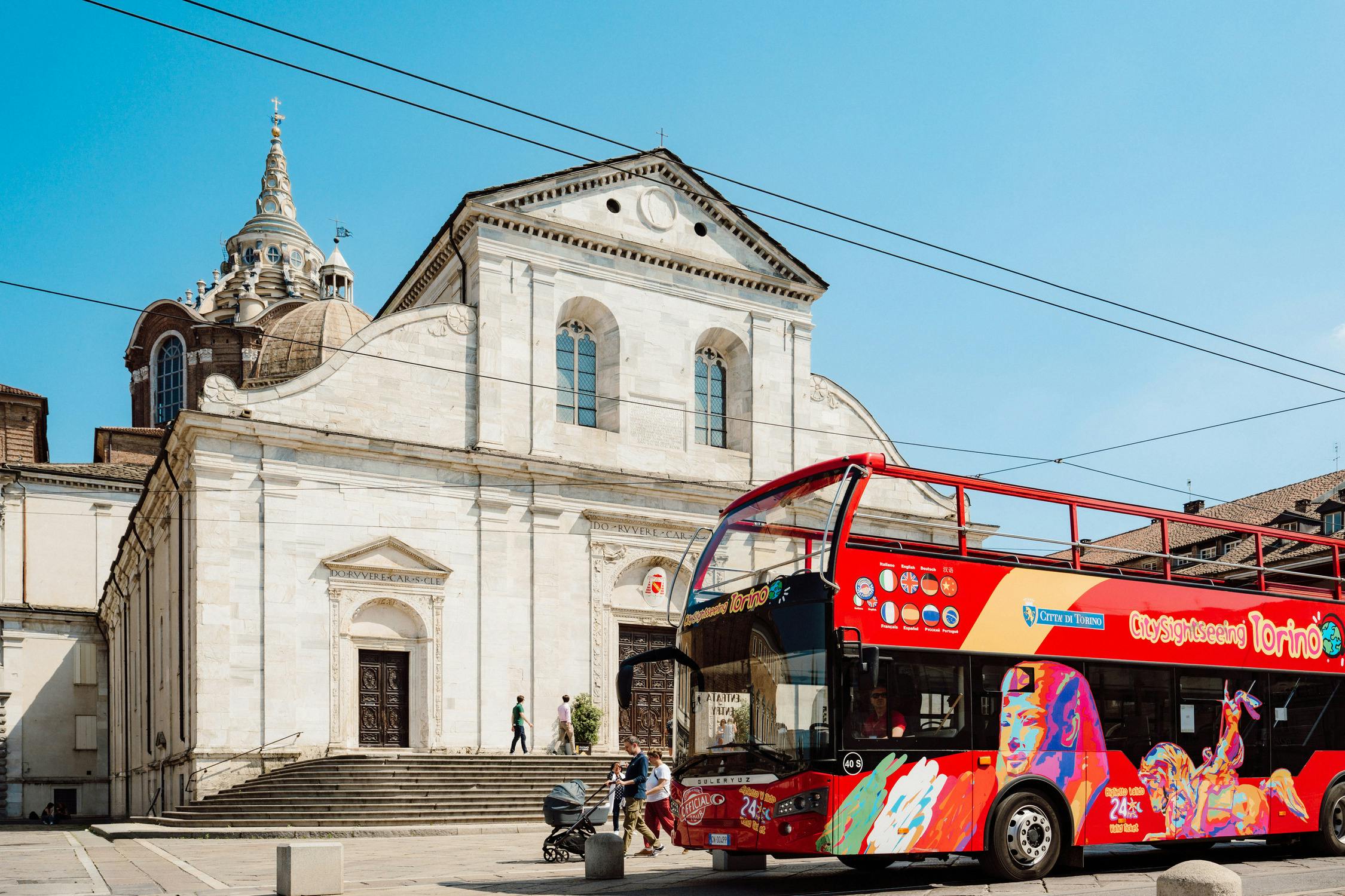 A red double-decker tour bus in front of a historic white building with arched windows on a sunny day.