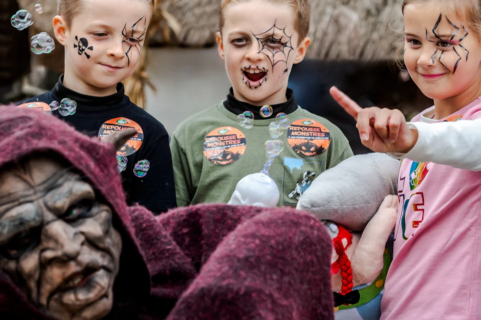 Children with face paint are interacting with a person in fancy dress, surrounded by bubbles, in an outdoor setting.