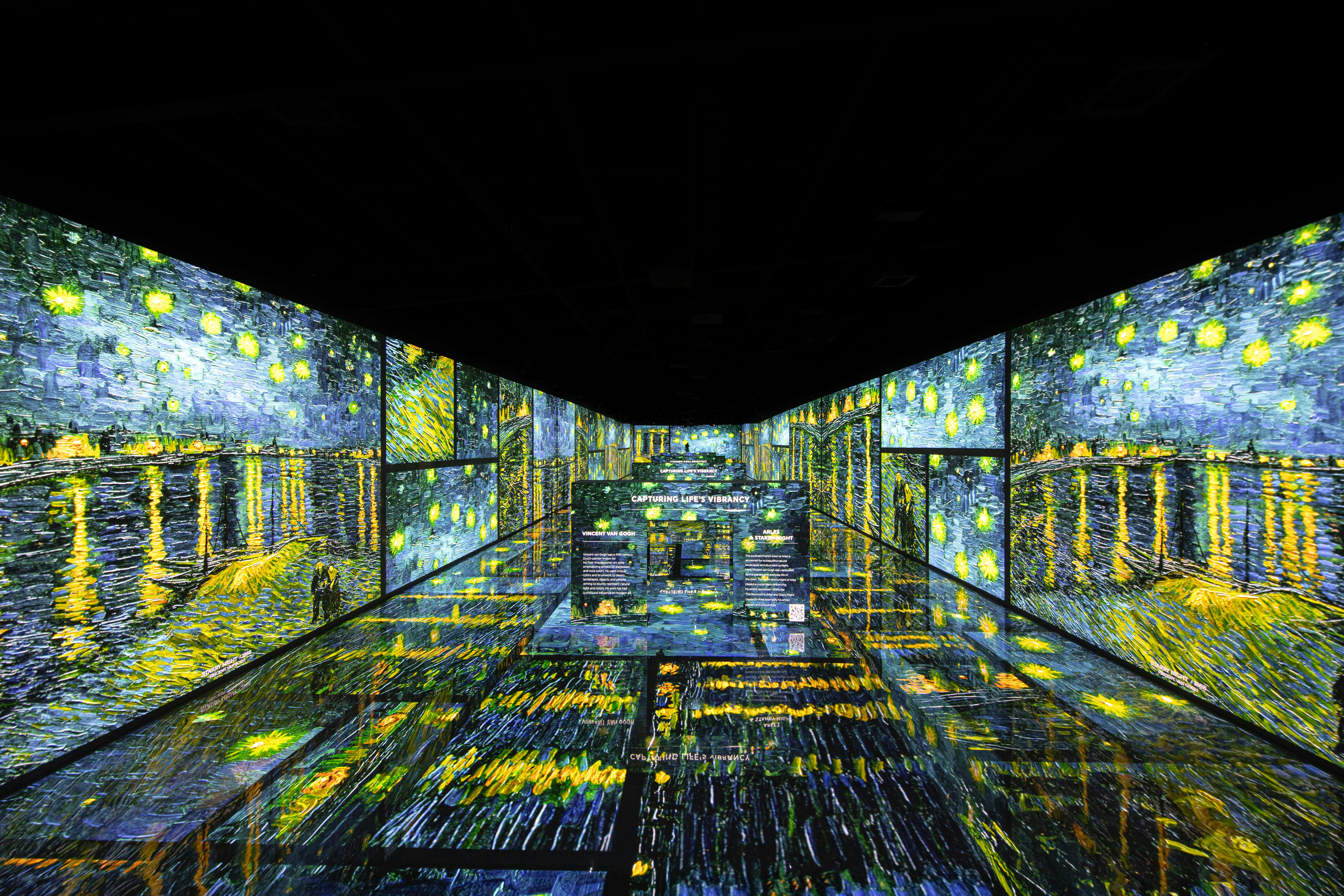 Pokój ze ścianami i podłogą pokrytą wciągającą, cyfrową sztuką Van Gogha z grafiką i panelami informacyjnymi w stylu „Gwiezdnej nocy”.