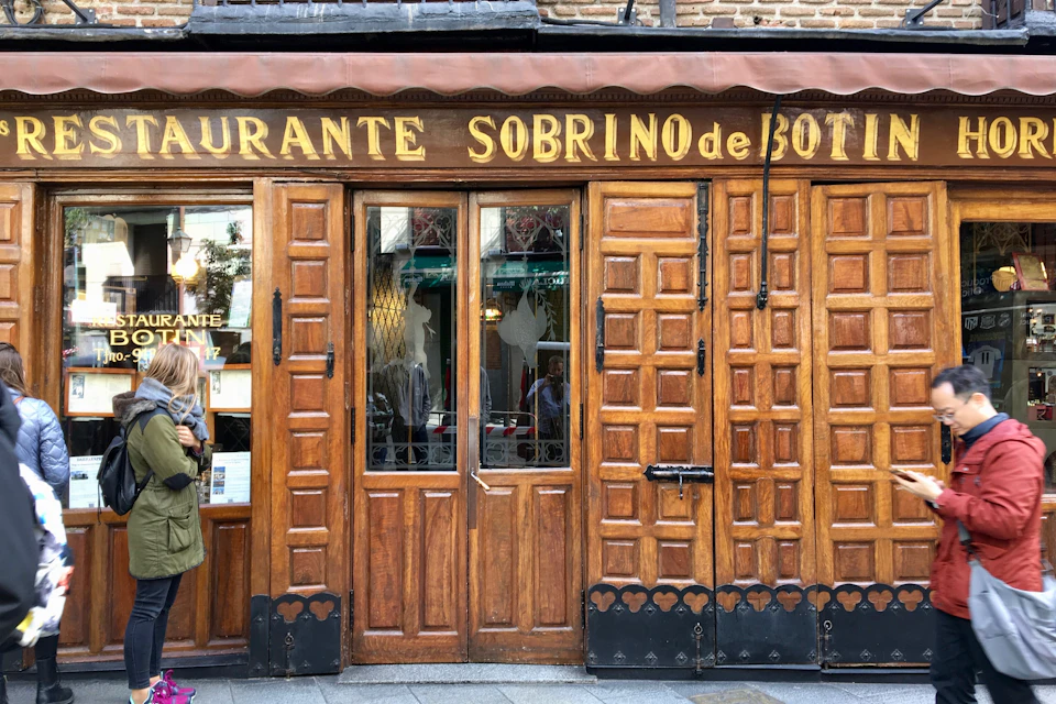 Wooden facade of Restaurante Sobrino de Botín with glass doors displaying reflections; person standing near the entrance.