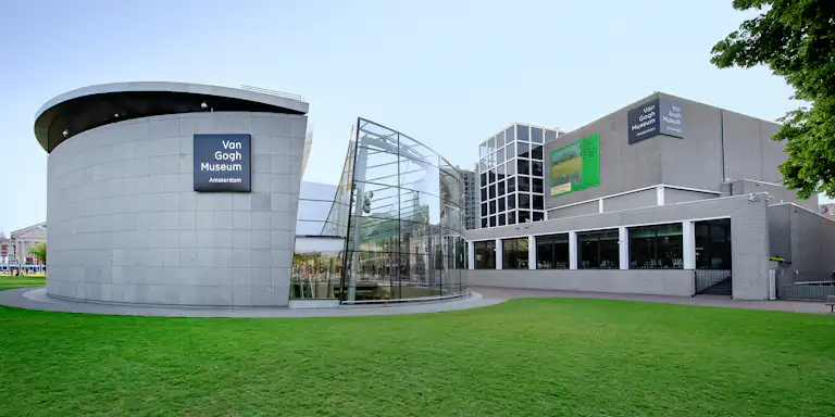 Vista exterior do Museu Van Gogh em Amesterdão, com uma arquitetura moderna com estruturas circulares e de vidro e um relvado verde.