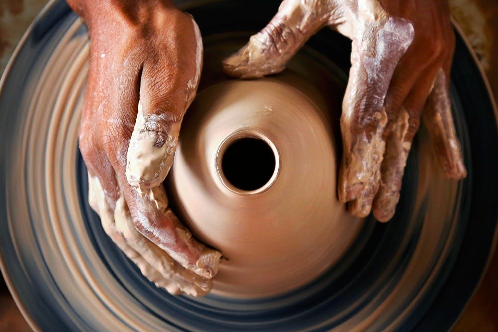 Close-up of hands shaping clay on a pottery wheel, forming a vase with a central opening.