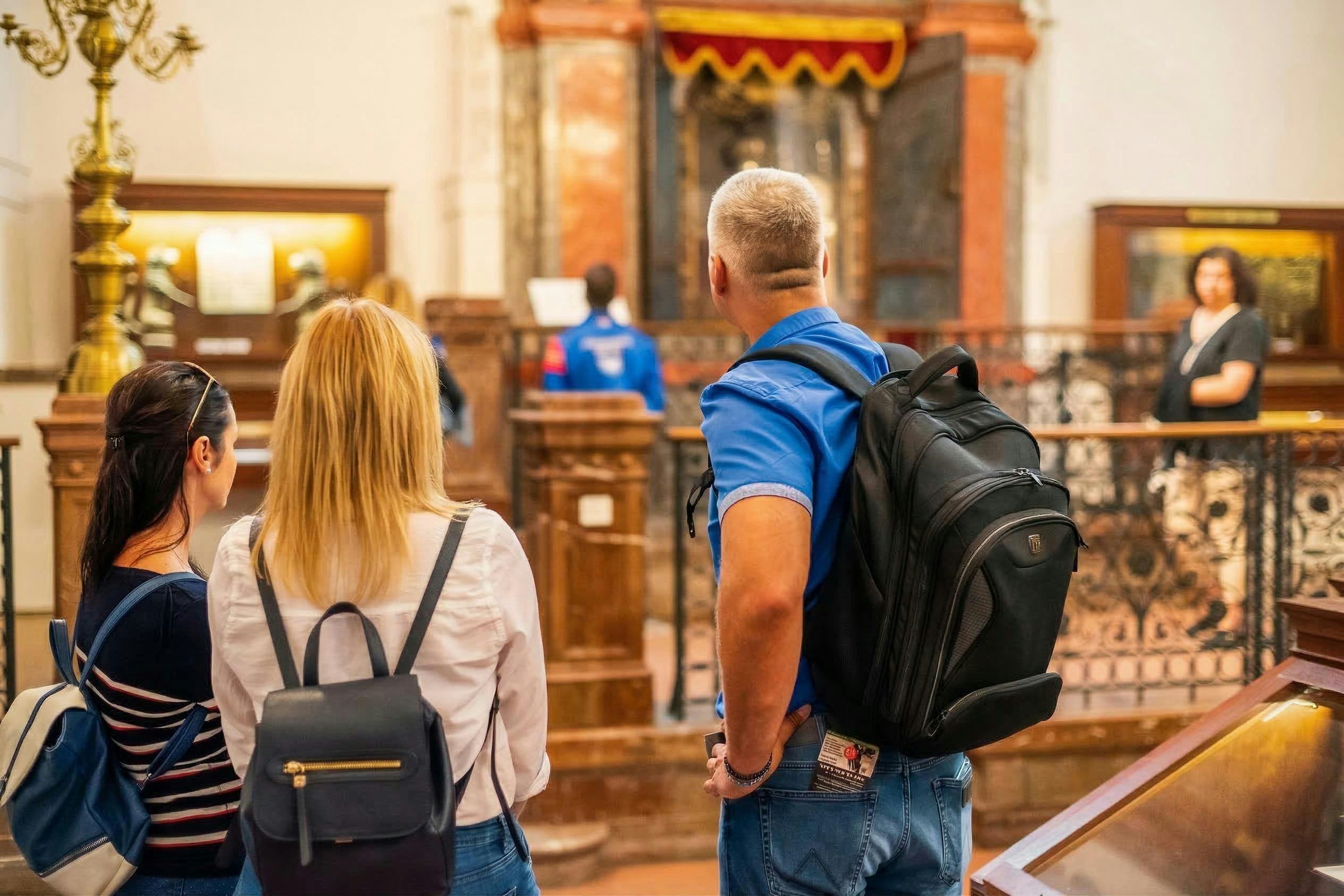 검은색 배낭을 맨 남성이 박물관에 서서 전시물을 보고 있으며, 다른 방문객과 장식품이 보입니다.