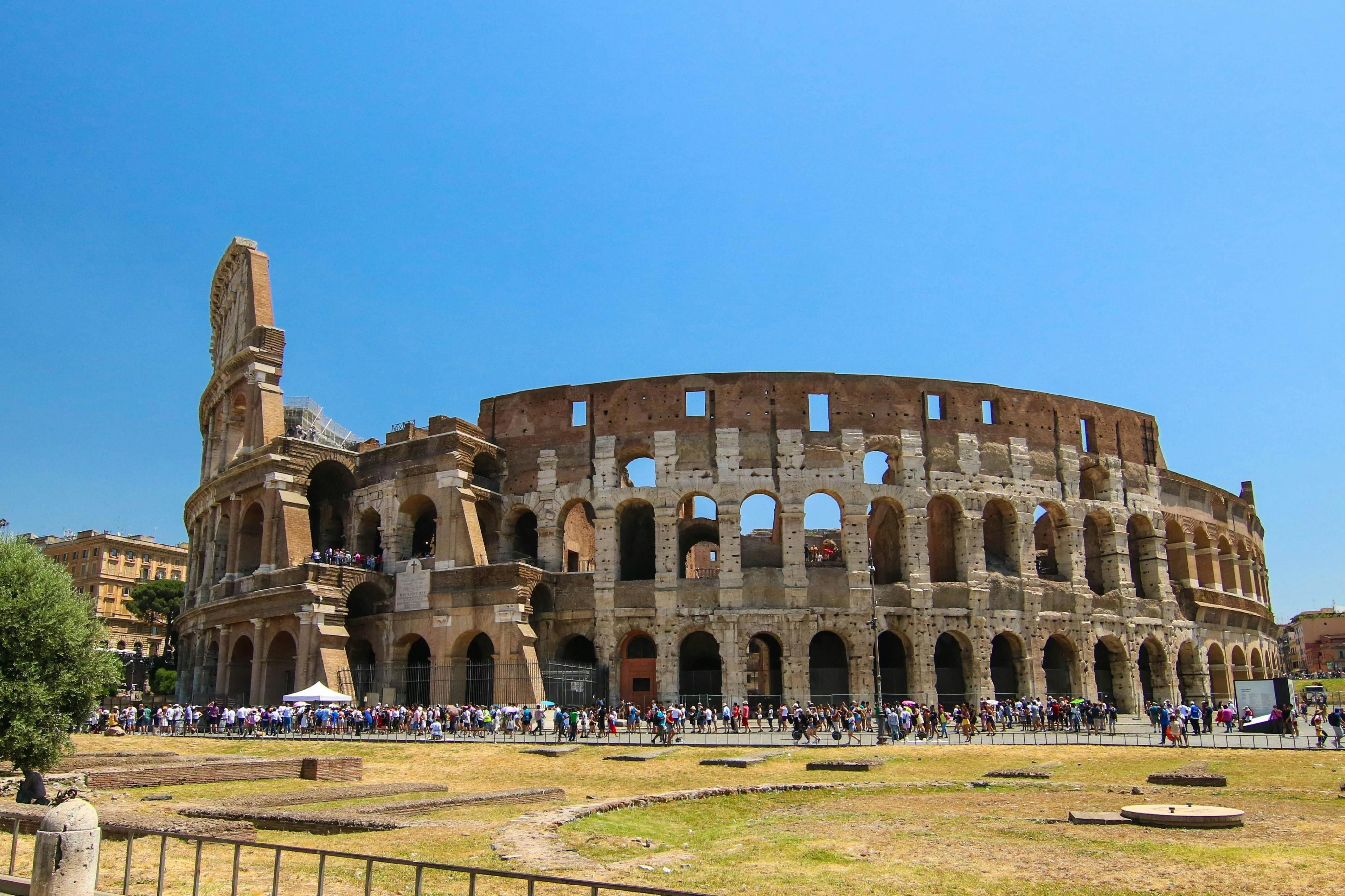 Une vue du Colisée à Rome sous un ciel bleu limpide, avec des touristes rassemblés à ses pieds.