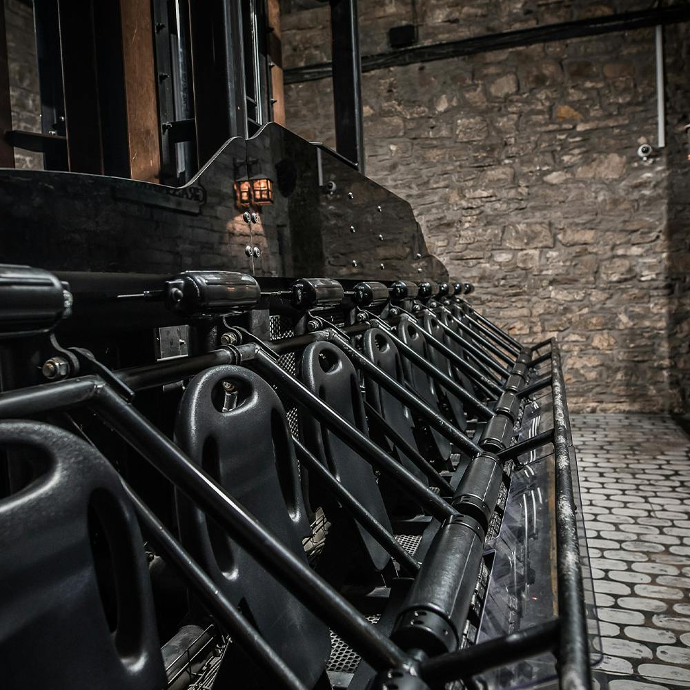 A row of black metal bars and seats inside a stone-walled industrial building with cobblestone flooring.