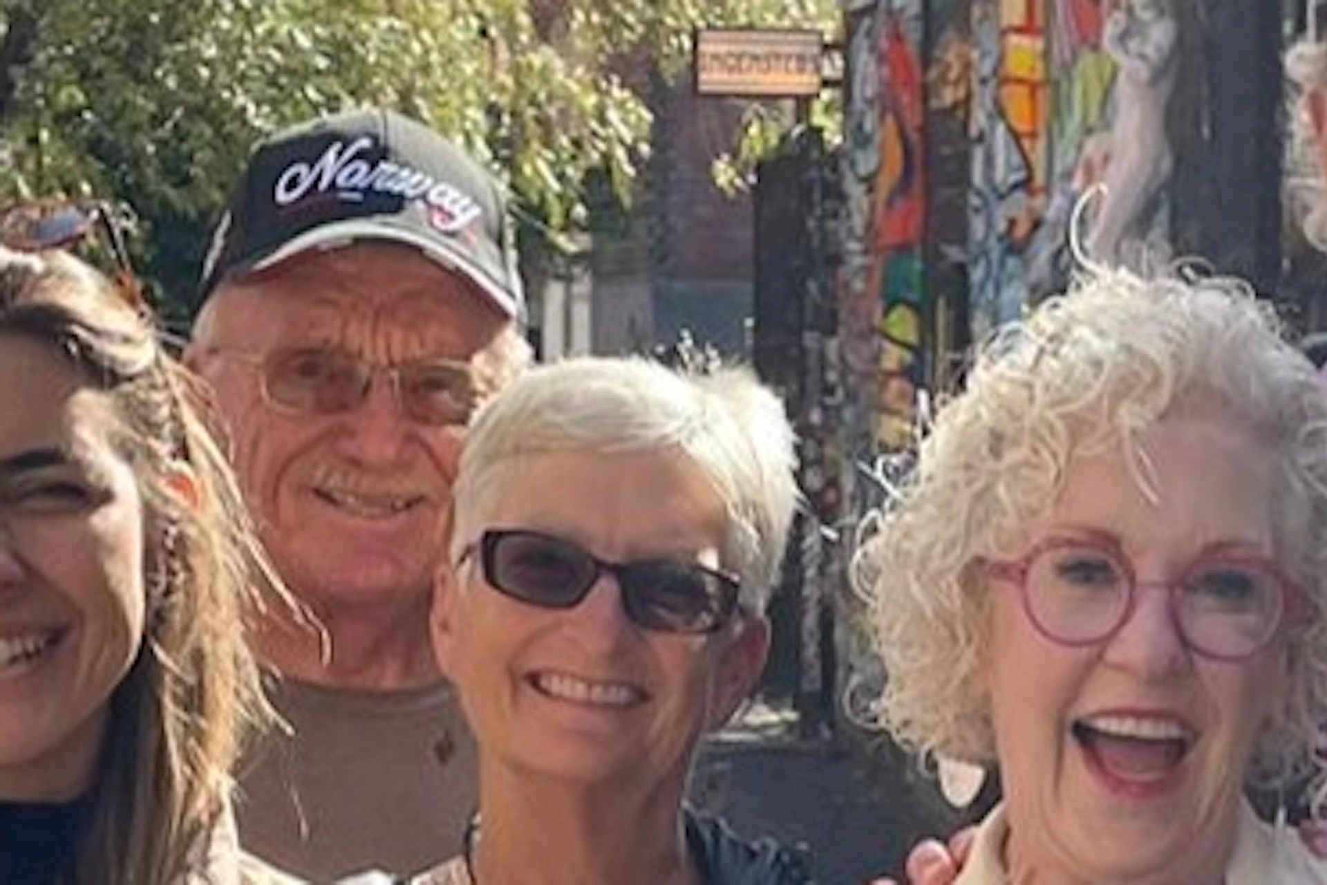 A group of nine people smiling and posing in a colorful alley with vibrant graffiti-covered walls.