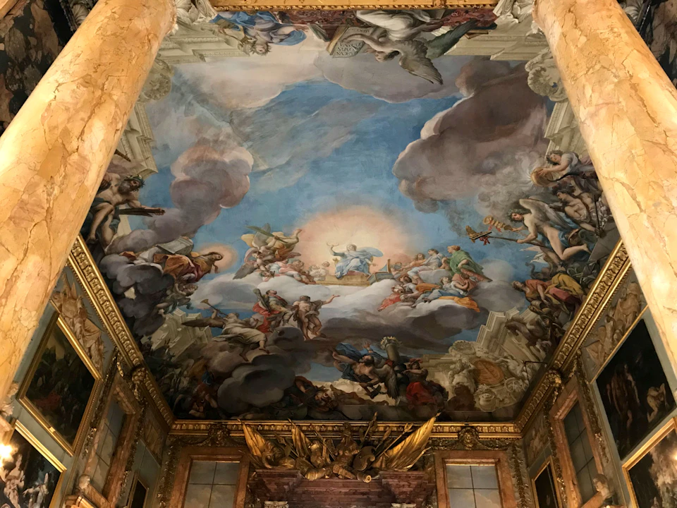Ornate ceiling fresco depicting a group of figures in a dramatic sky scene, surrounded by detailed architectural elements.