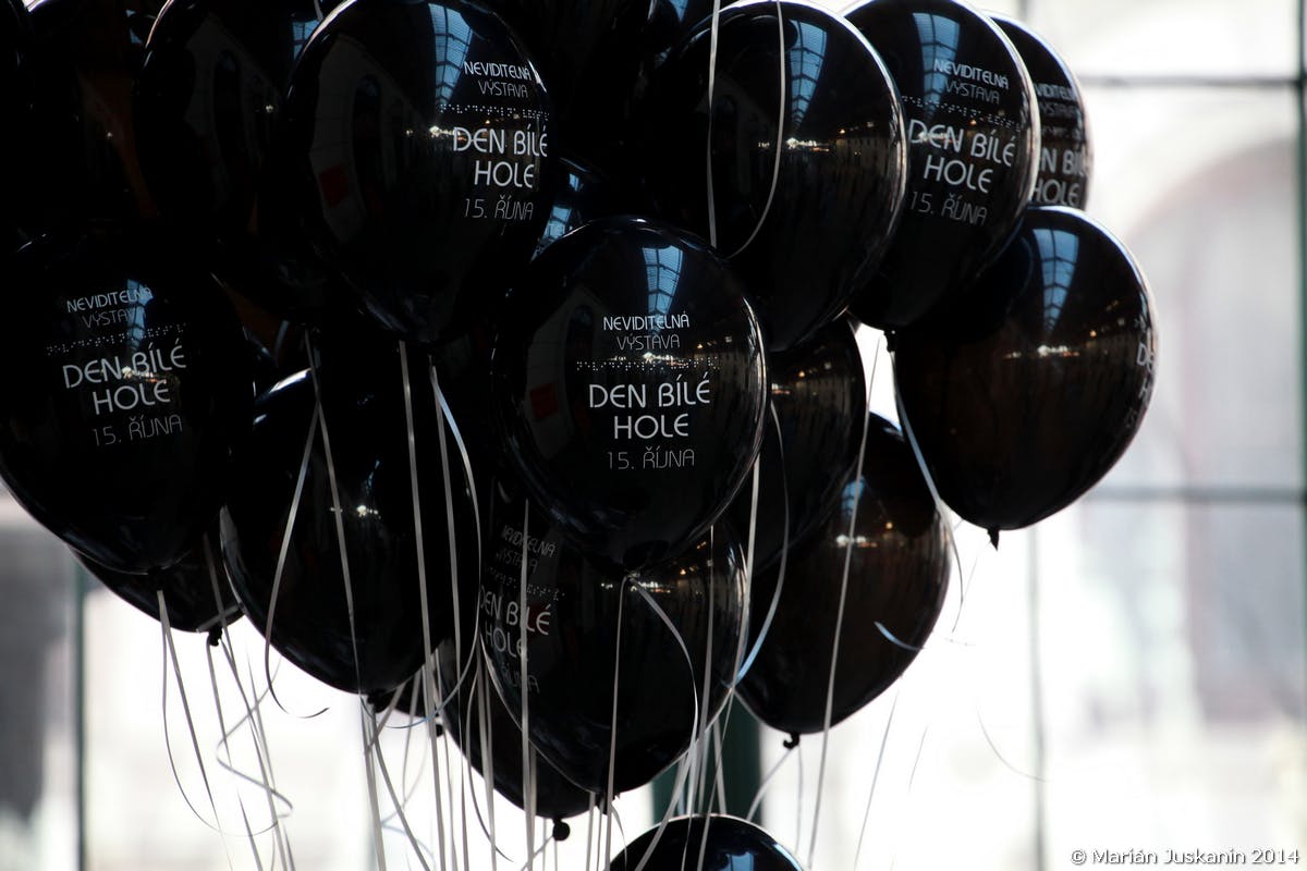 Une grappe de ballons noirs avec un texte blanc, chacun attaché à une ficelle blanche, reflétant les lumières intérieures et le plafond.