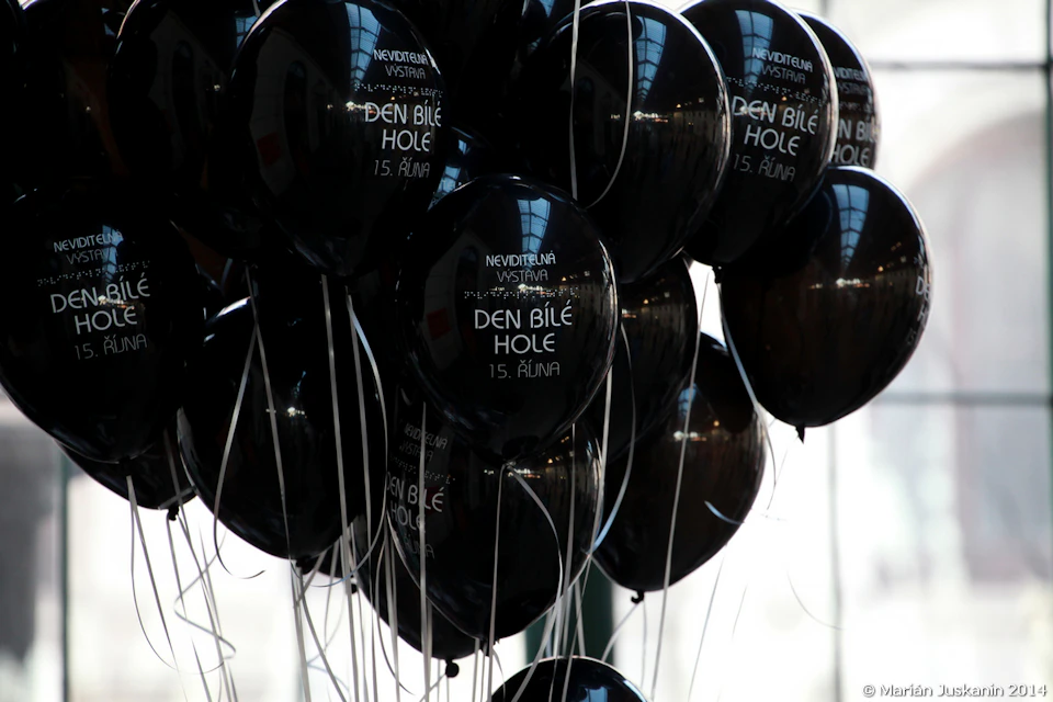 A cluster of black balloons with white text, each attached to white strings, reflecting indoor lights and ceiling.