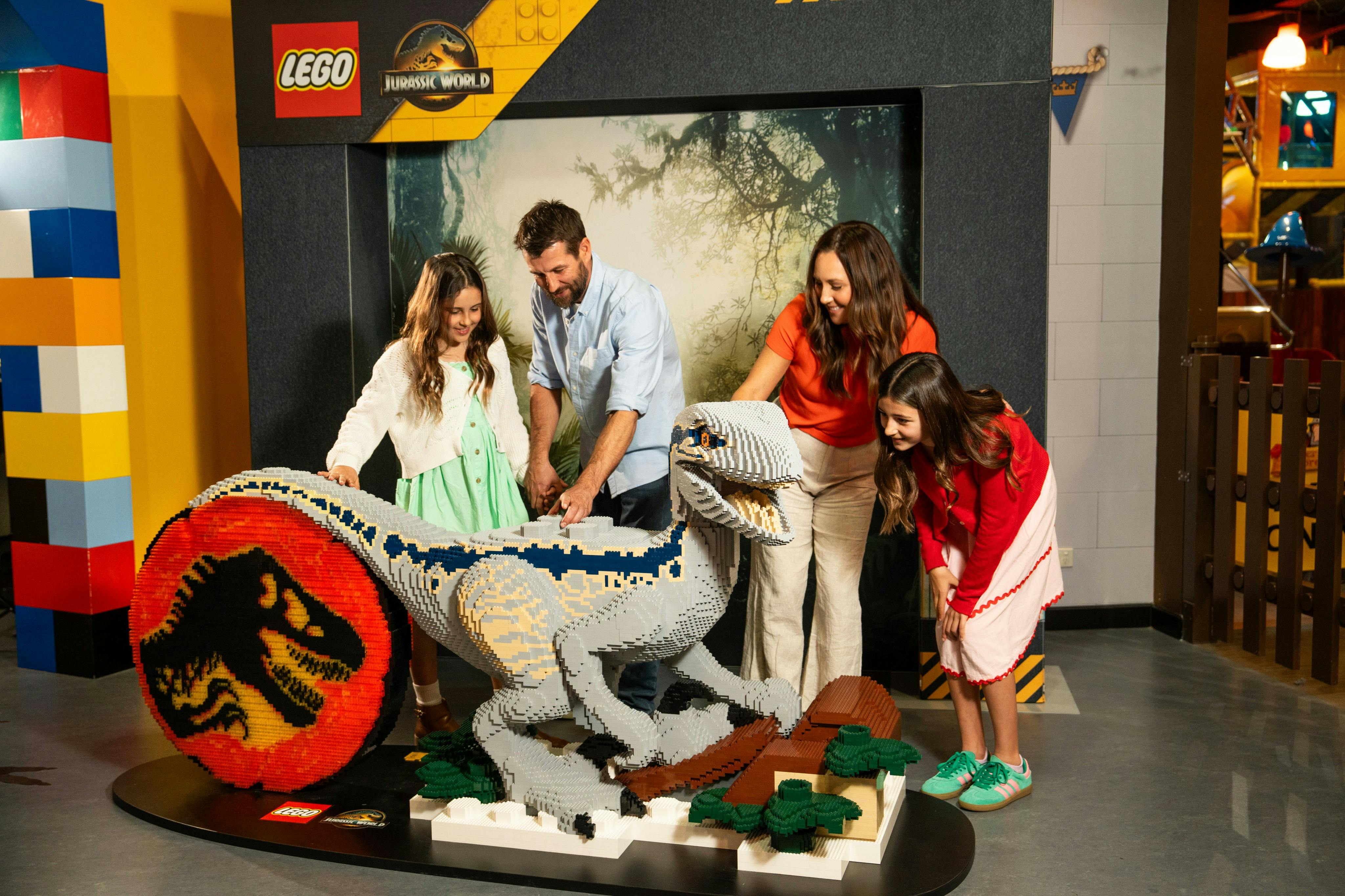 En familie på fire beundrer en LEGO-skulptur af en dinosaur fra Jurassic World, der vises i en temautstilling.