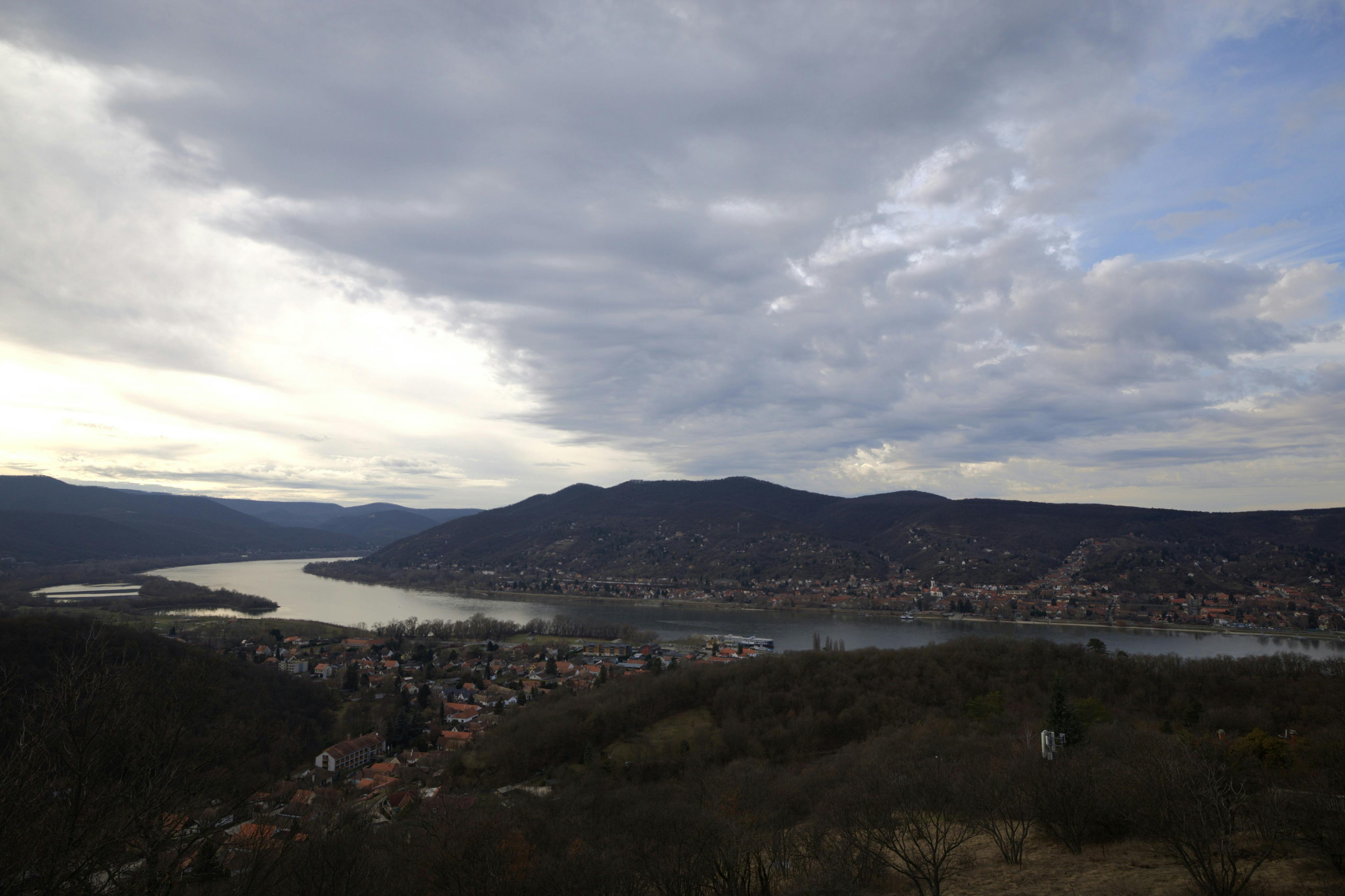 Vista panorámica de un río que serpentea por un paisaje de colinas, con una ciudad y un cielo nublado al fondo.