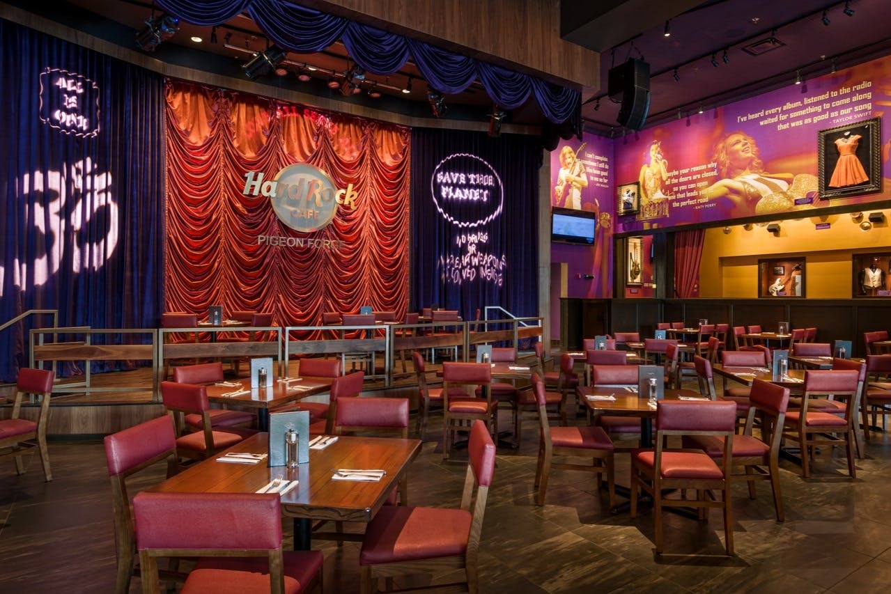 Empty dining area with red chairs and wooden tables in Hard Rock Cafe, Pigeon Forge. Stage with red curtains and neon sign.