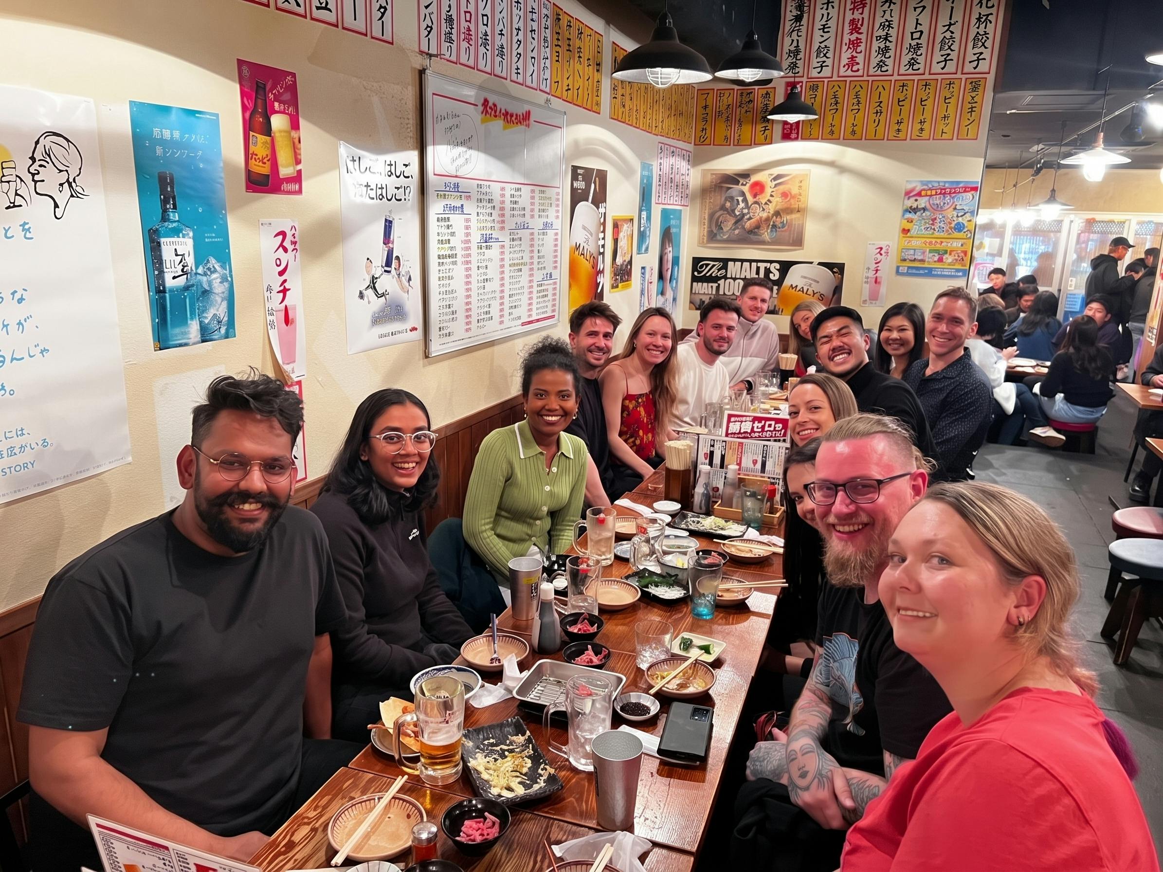 A group of people seated around a table in a restaurant, smiling and enjoying food and drinks.