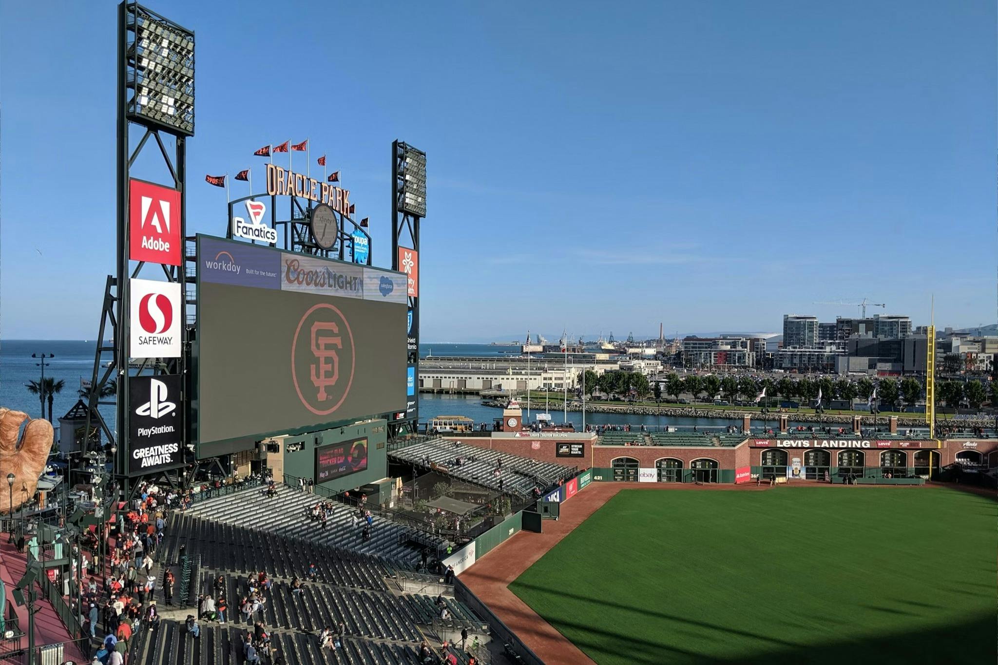 Baseballový stadion s velkou výsledkovou tabulkou s logem San Francisco Giants s panoramatem města a zálivem v pozadí.