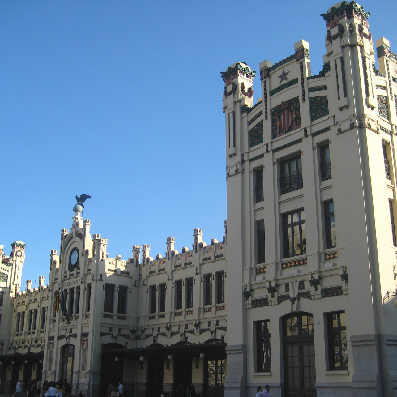 A grand art deco building with tall towers, ornate decorations, and a clock on the facade against a clear blue sky.