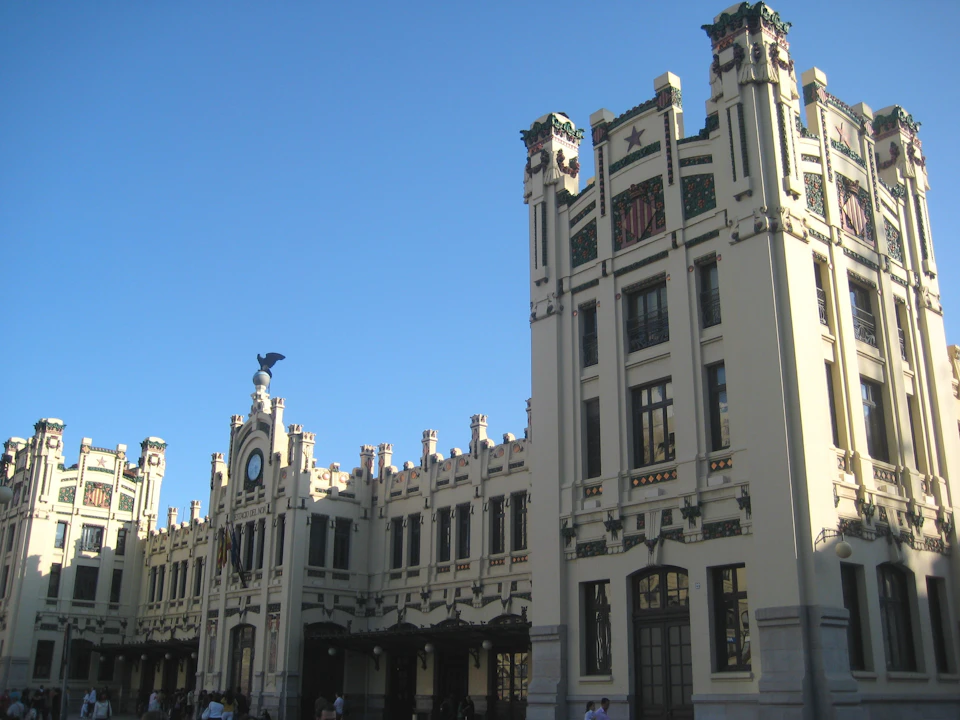 A grand art deco building with tall towers, ornate decorations, and a clock on the facade against a clear blue sky.