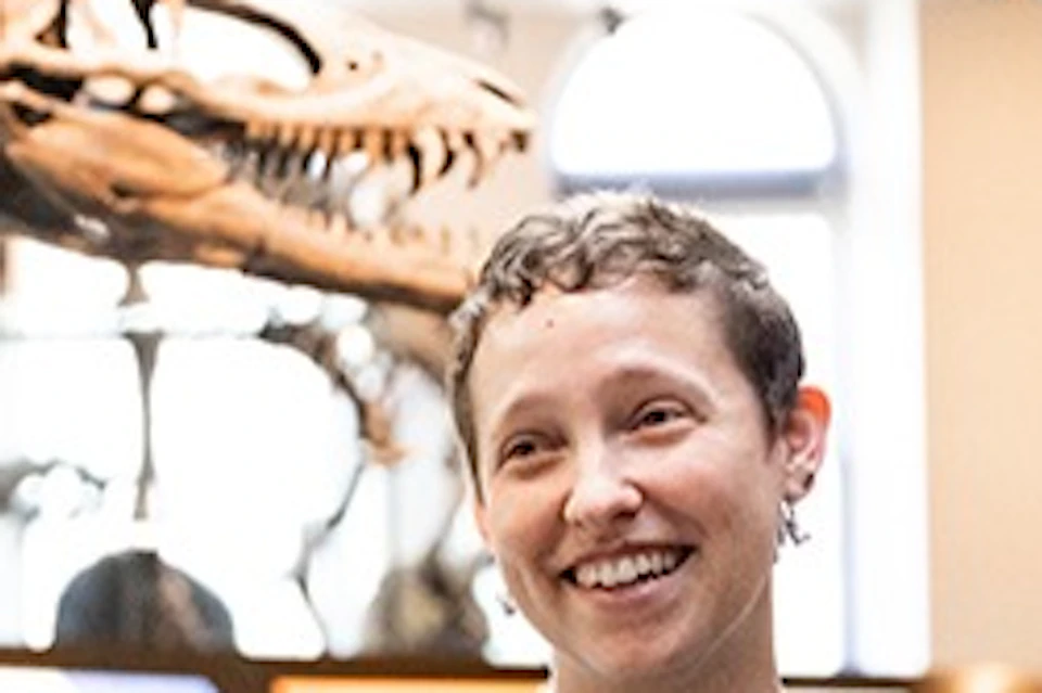A group of people in a museum exhibit with dinosaur skeletons, one person wearing a badge appears to be explaining something.