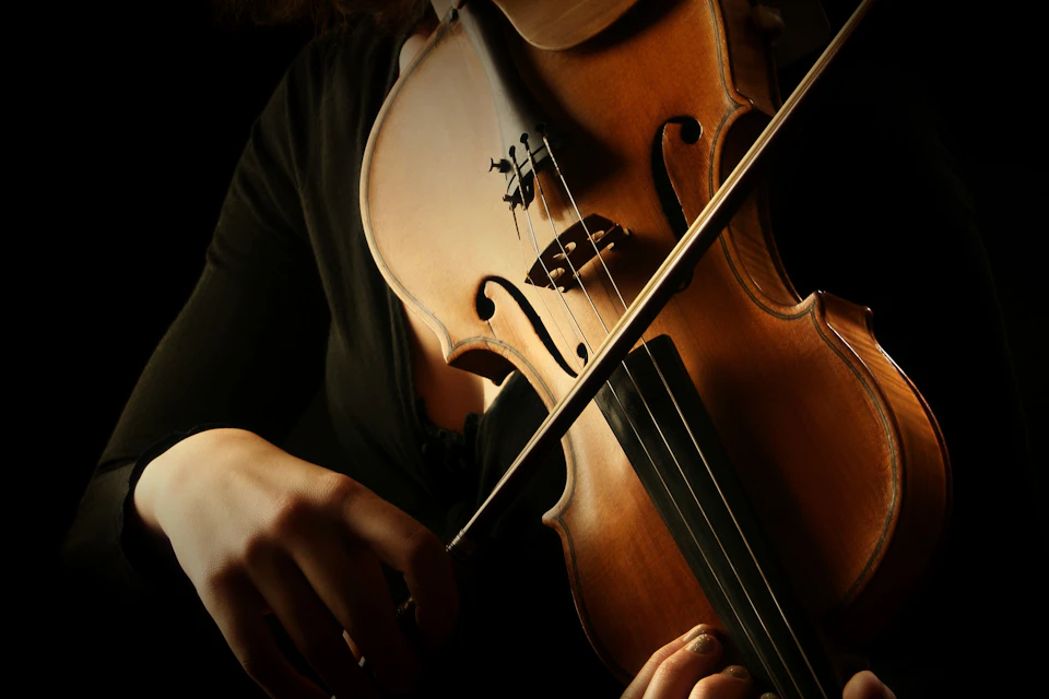 Close-up of a person playing a violin, highlighting the instrument and the bow in motion under warm lighting.