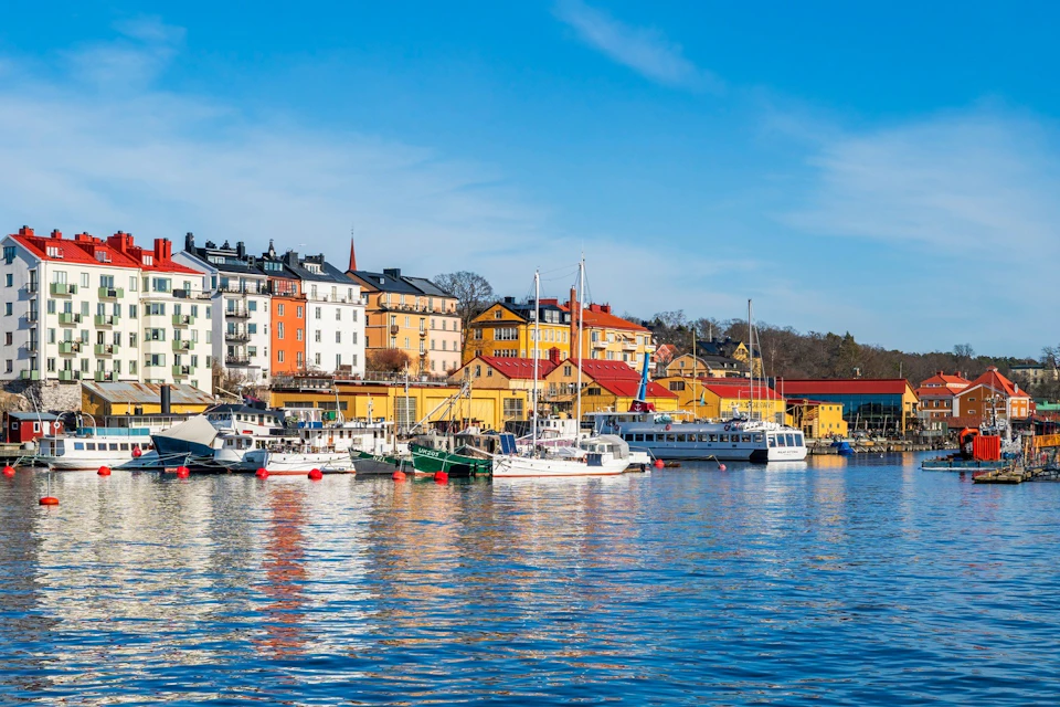 Colourful buildings and boats line a tranquil waterfront beneath a blue sky.