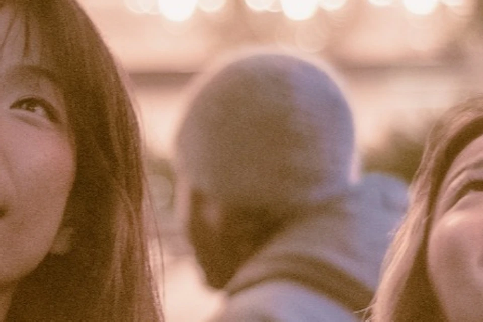 Two people look up and smile under warm, glowing lights in a festive indoor setting.