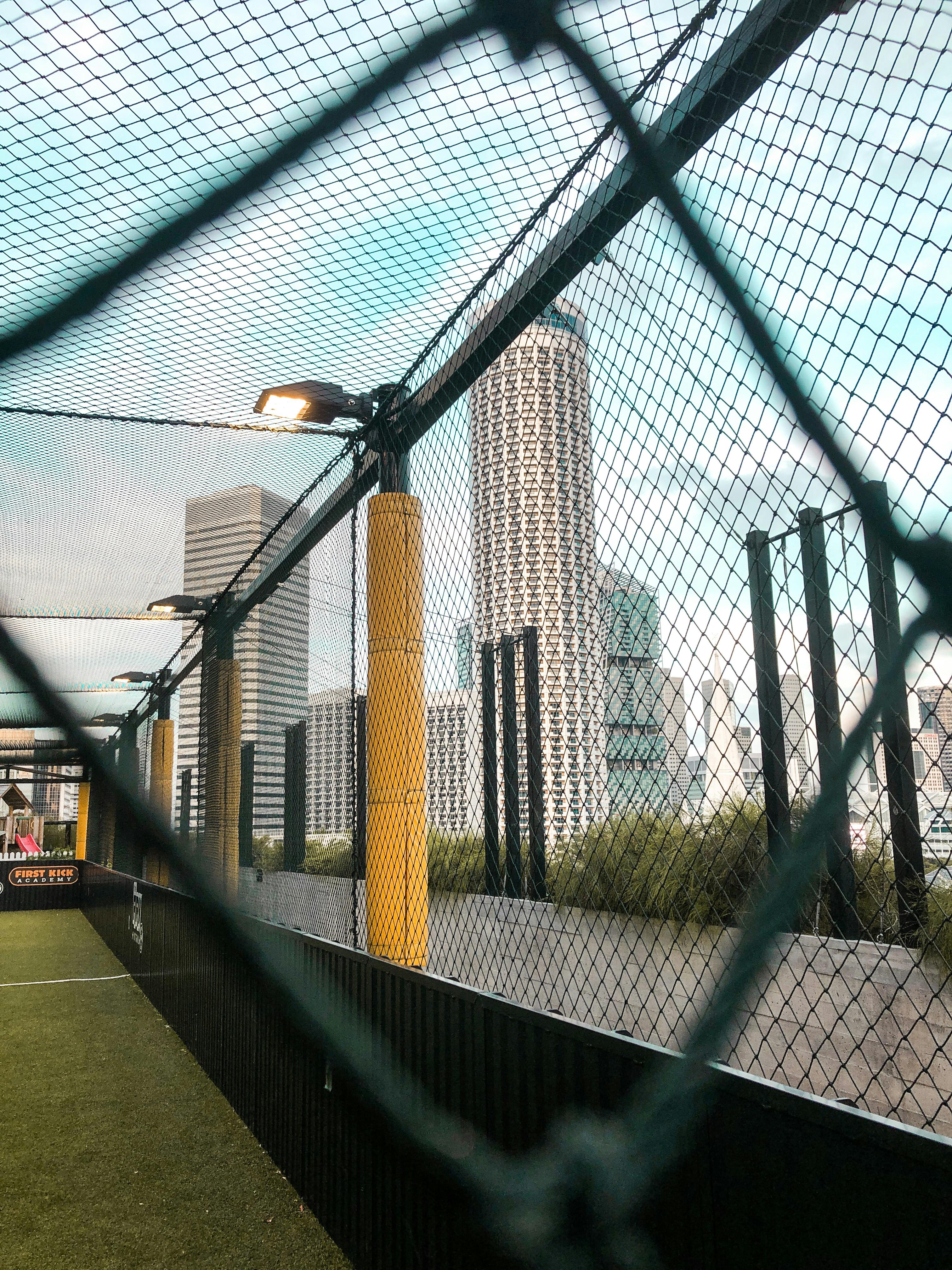 Campo da calcio sopraelevato con rete, incorniciato da alti edifici e grattacieli in un contesto urbano.