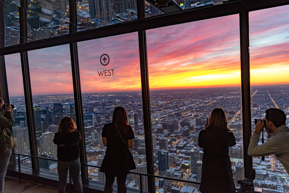 tourists gazing at chicago cityscape below at the top of 360 Chicago observatory