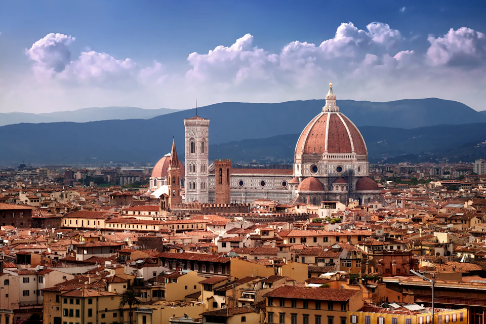 Skyline of Florence, Italy, featuring the dome and bell tower of the Florence Cathedral (Duomo) against a mountain backdrop.