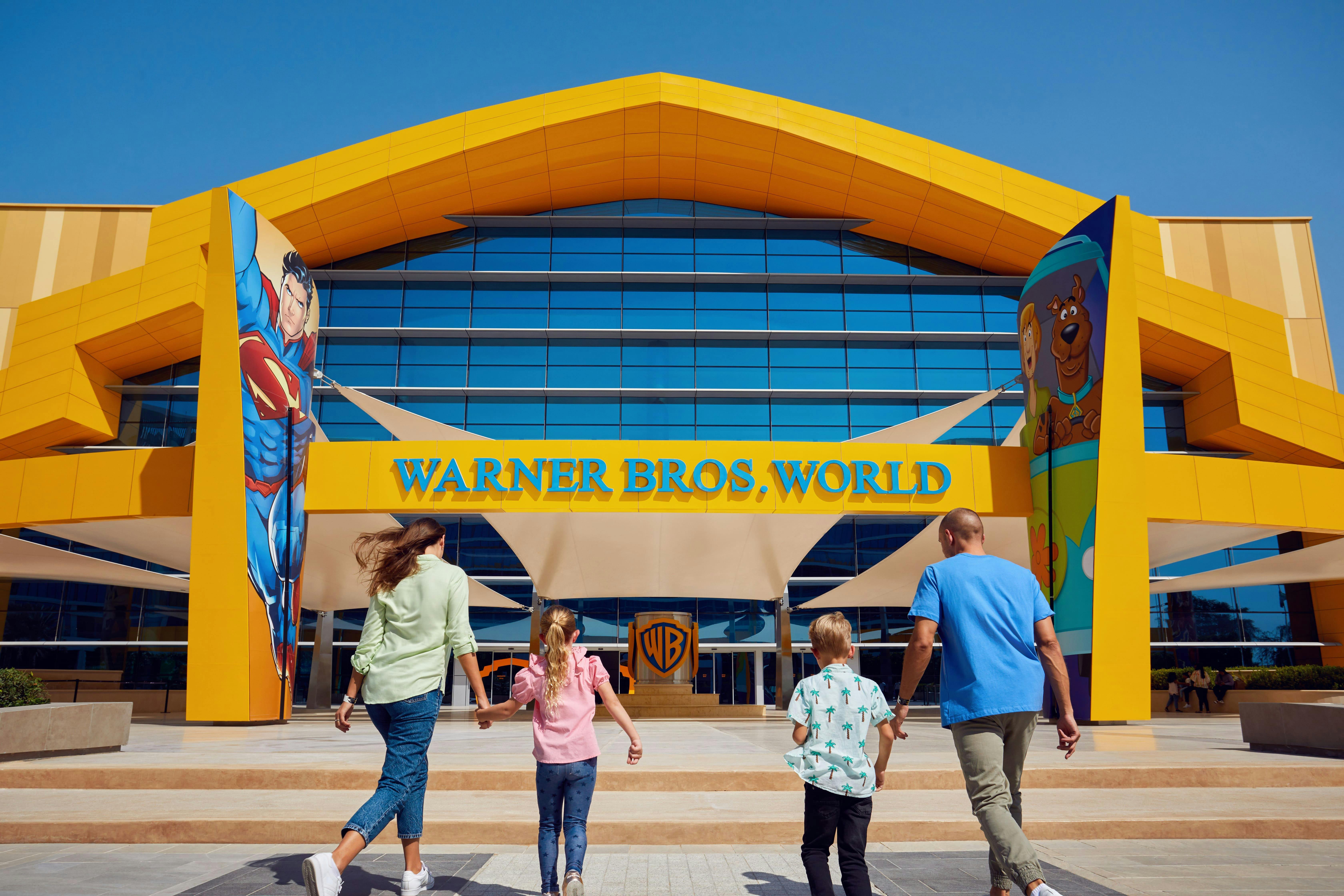 Une famille se dirigeant vers l'entrée de Warner Bros. World, avec des illustrations de Superman et de Scooby-Doo sur la façade du bâtiment.