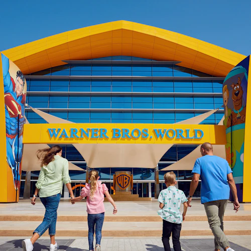 Eine Familie auf dem Weg zum Eingang von Warner Bros. World, mit Superman- und Scooby-Doo-Kunstwerken an der Fassade des Gebäudes.