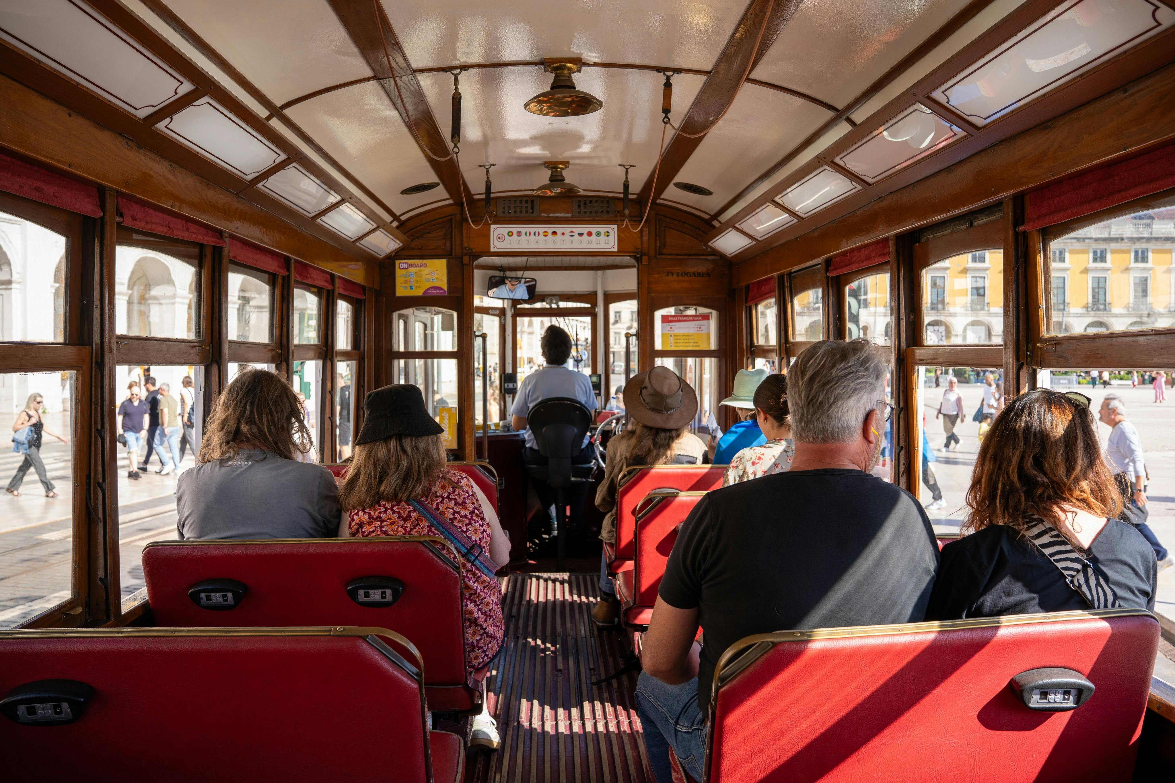 빨간색 좌석에 승객이 앉아 있고, 앞에 운전자가 있으며, 창문을 통해 햇빛이 흐르는 트램의 내부.