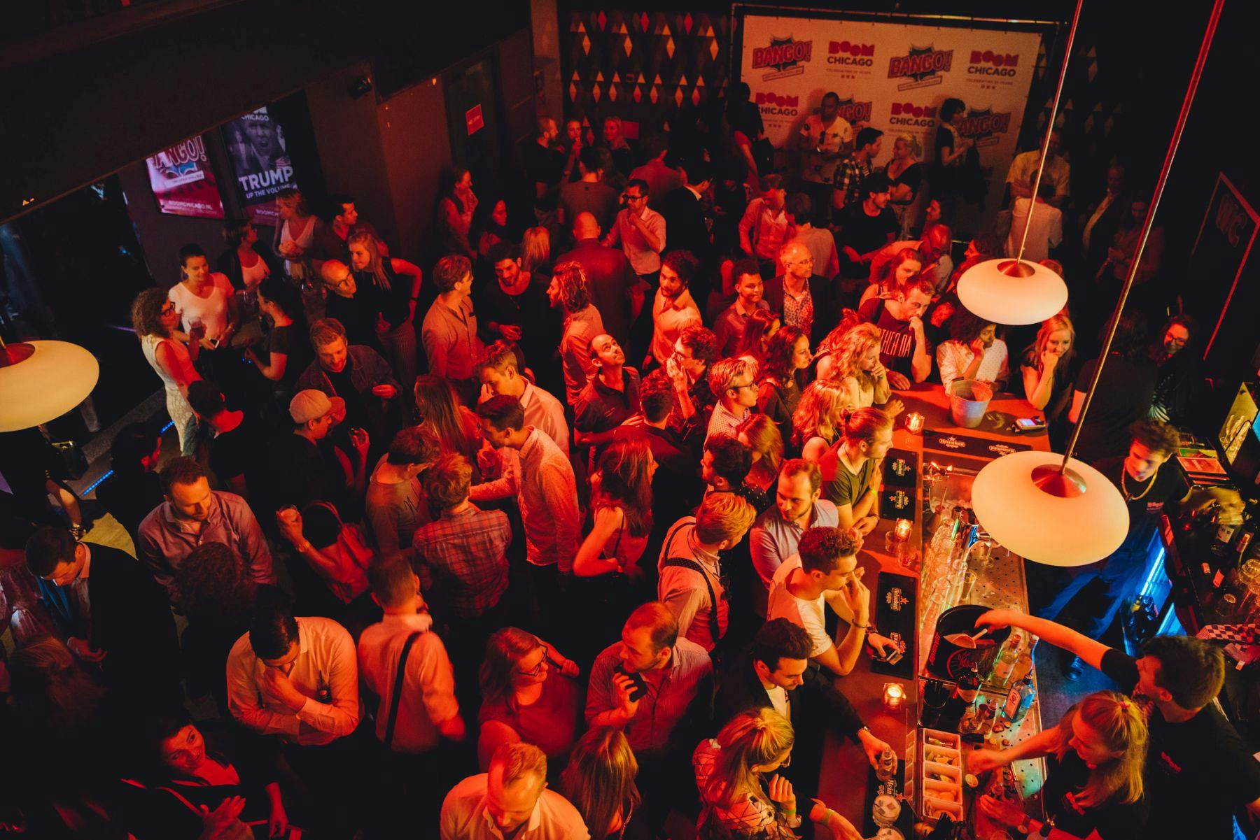 Eine belebte Partyszene in einem Innenraum mit Menschen, die unter warmer roter Beleuchtung zusammenkommen.