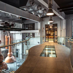 Modern industriell interiör med stora kopparställ, glasväggig gångväg, synliga rör och upplyst rum märkt "1066" i bakgrunden.