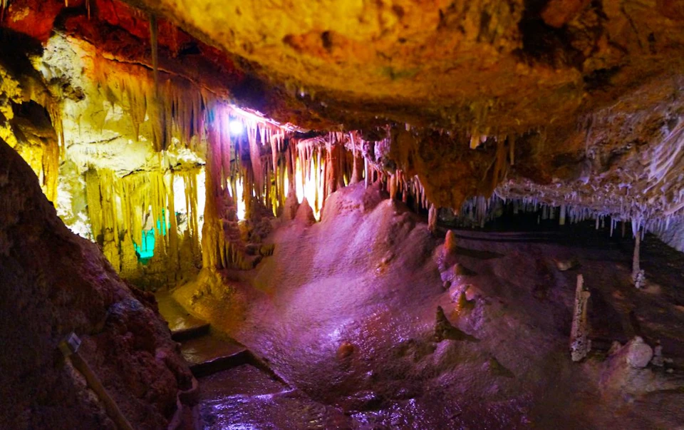 Cave with illuminated stalactites and stalagmites, colorful lights reflecting off the rocky surfaces.