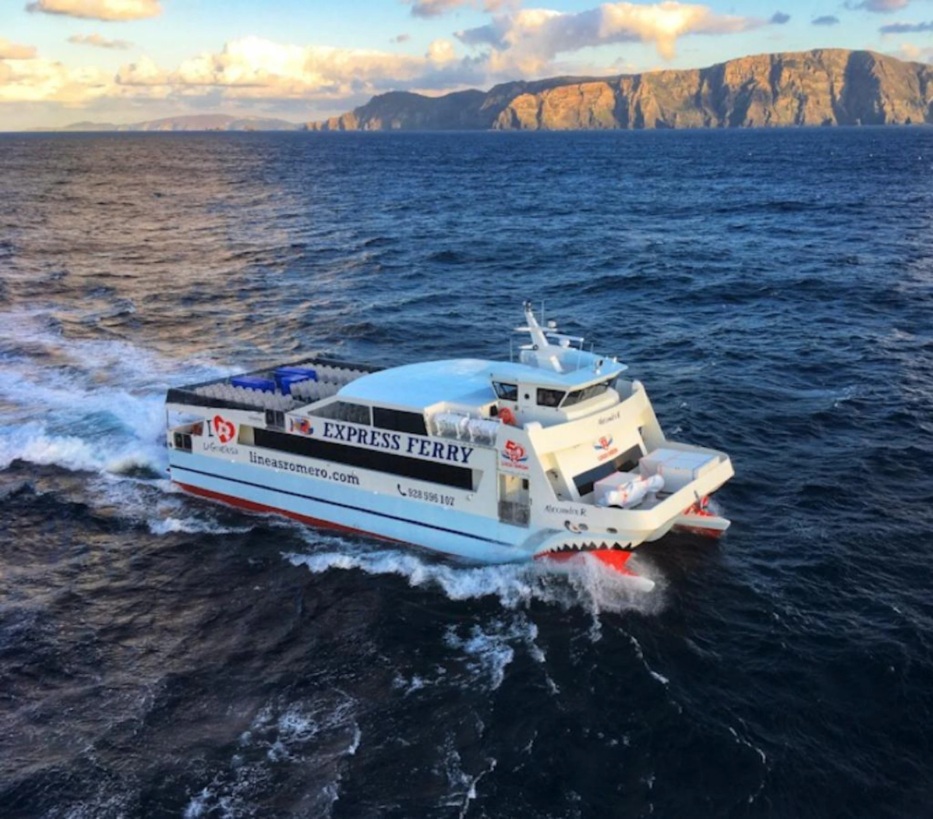 A white and red ferry labeled "Express Ferry" travels over a blue ocean, with a rocky cliff coastline in the background.