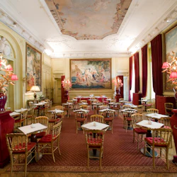 Påkostad matsal med röda sammetsstolar, marmorbord, utsmyckad belysning och stora klassiska målningar som pryder väggarna och taket.