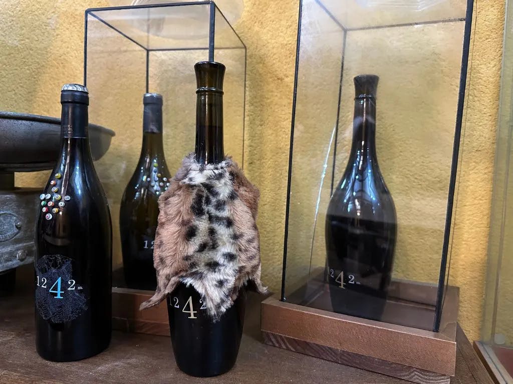 動物の毛皮で覆われたワインボトルが、同様のボトルを背景にしたガラスケースに展示されています。