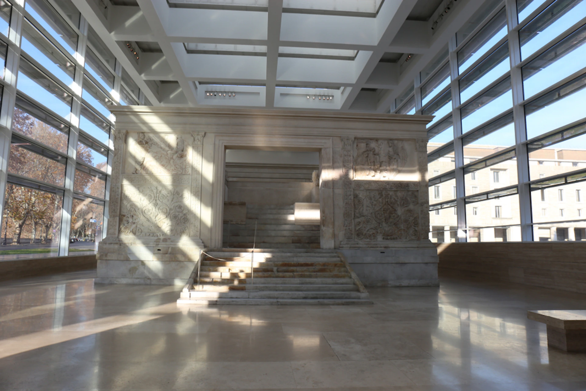An ancient stone structure with intricate carvings, set in a modern glass and steel building with large windows and skylights.