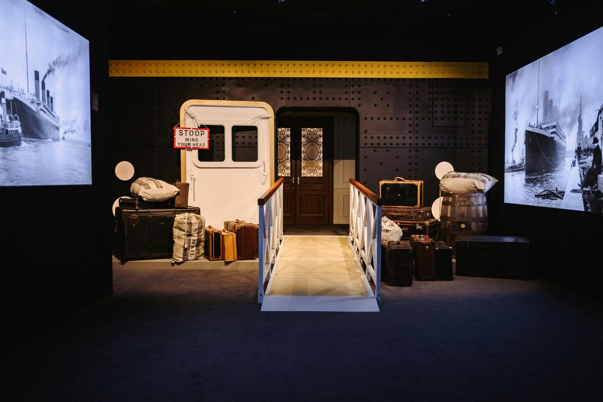 A ship-themed exhibition setup featuring a gangway leading to a door, with luggage and barrels on either side.