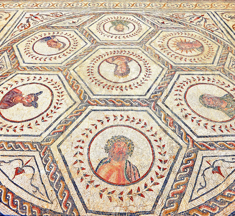 Intricate mosaic floor with hexagonal patterns depicting various human and animal figures surrounded by decorative borders.