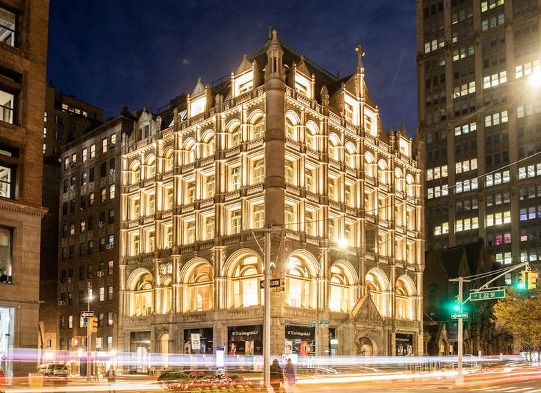 Φωτισμένο, περίτεχνο πολυώροφο κτίριο σε μια γωνία του δρόμου της πόλης τη νύχτα με φωτεινά μονοπάτια από τη διερχόμενη κυκλοφορία.