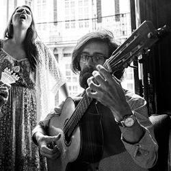 Svartvitt foto av två män som spelar gitarr medan en kvinna står mellan dem och sjunger passionerat med slutna ögon.