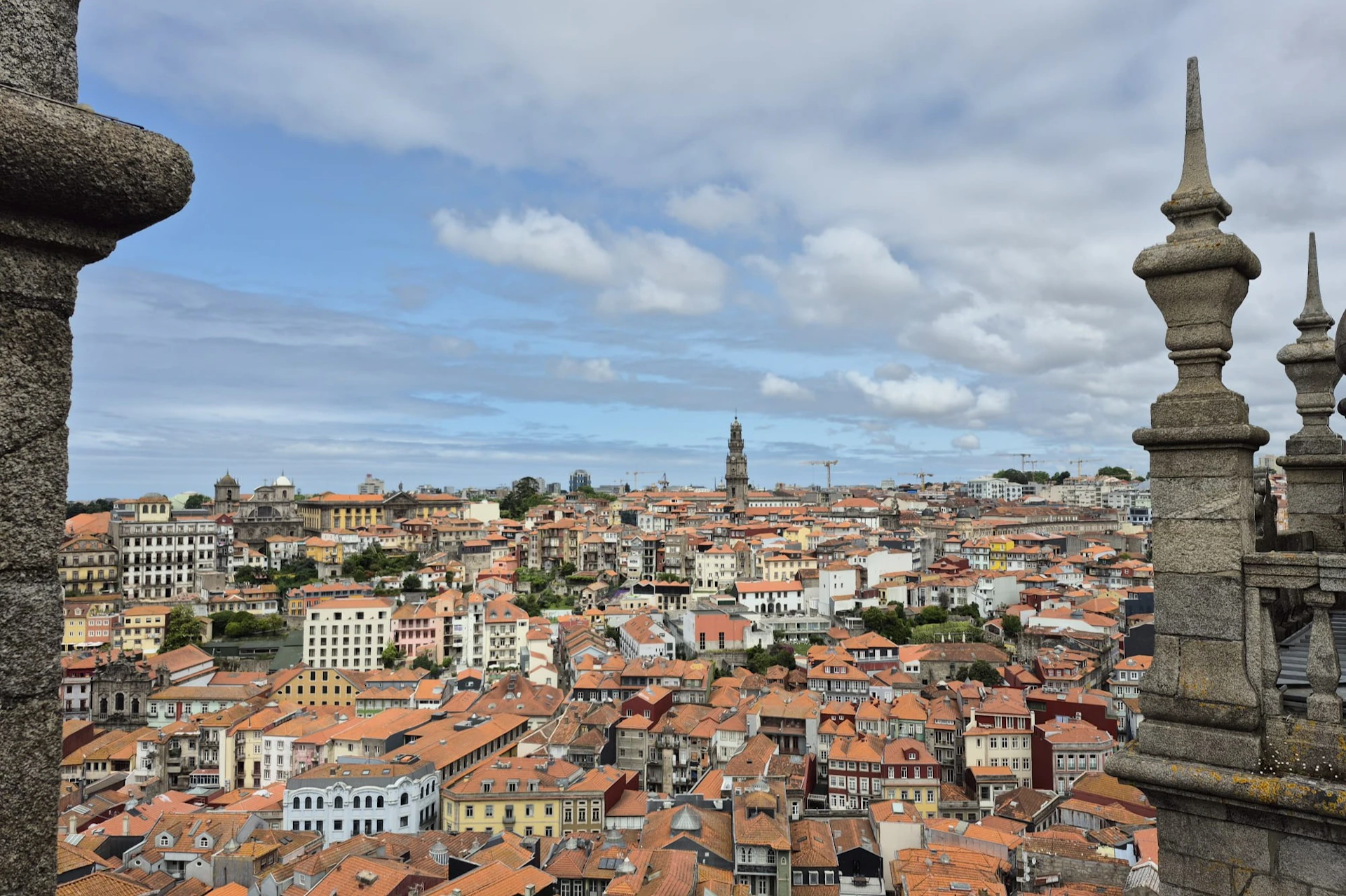 A cityscape with red-roofed buildings and a tall clock tower under a partly cloudy sky.