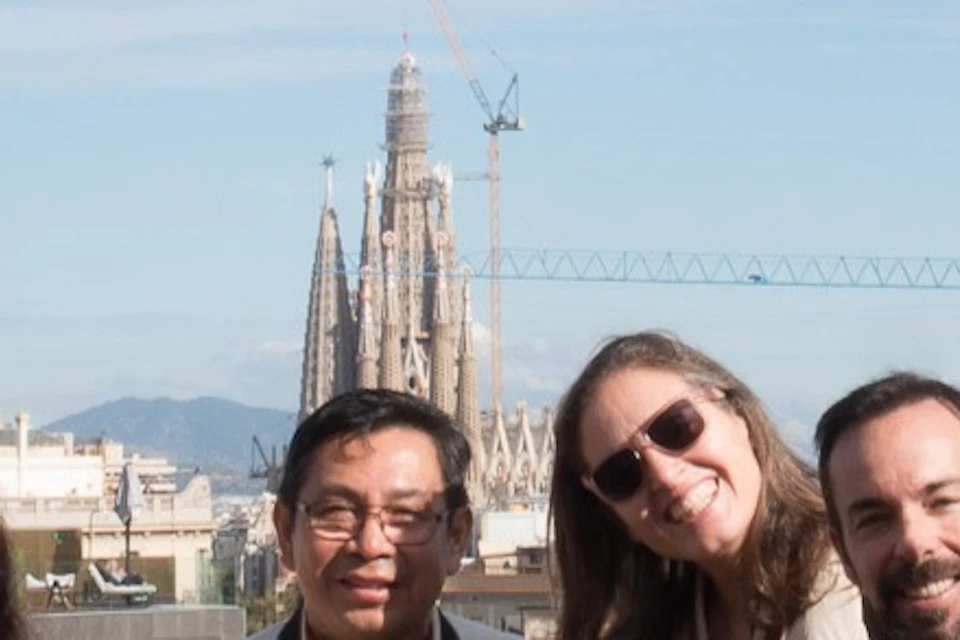 A group of people posing for a photo under an archway with a cityscape and a cathedral in the background.