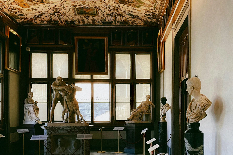 A room in a museum with marble statues, including one depicting a group of wrestling figures, and detailed frescoes on the ceiling.