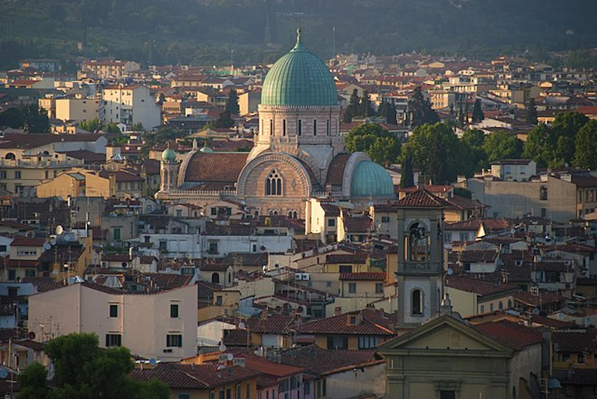 A cityscape featuring a large domed building and numerous terracotta-roofed structures under a hilly backdrop.